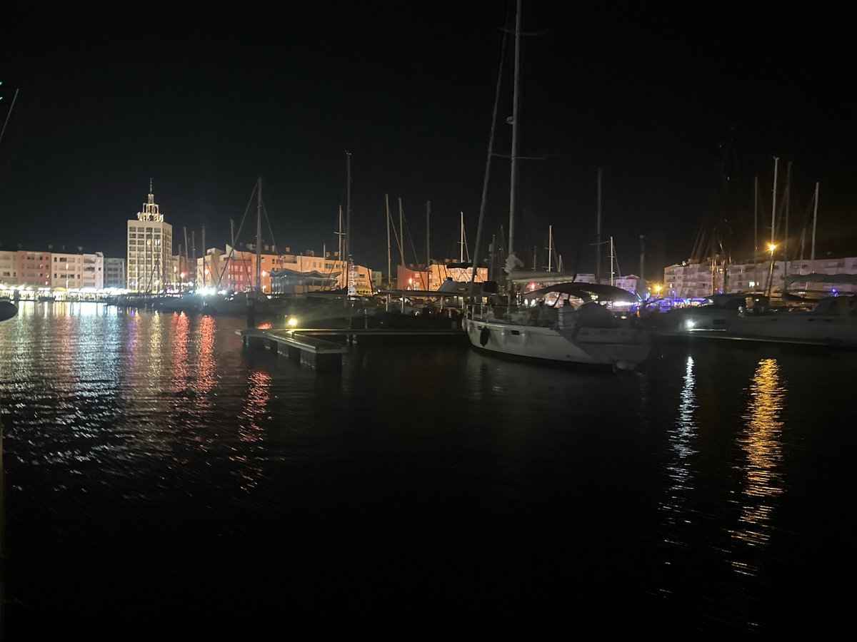 Agde marina at night: Ferris wheel, boats, and a street performer