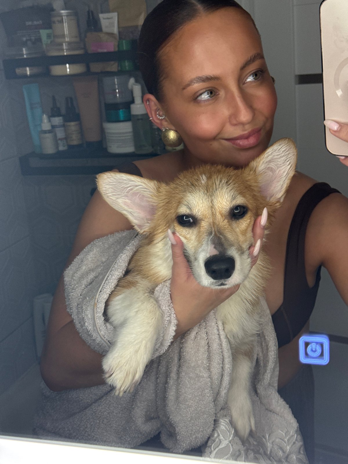 Woman takes bathroom selfie with towel-wrapped corgi puppy