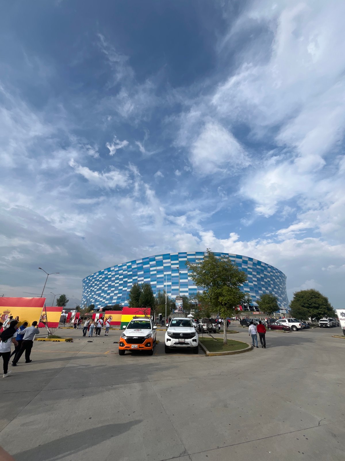 Modern stadium with checkered facade observed with flags, vehicles