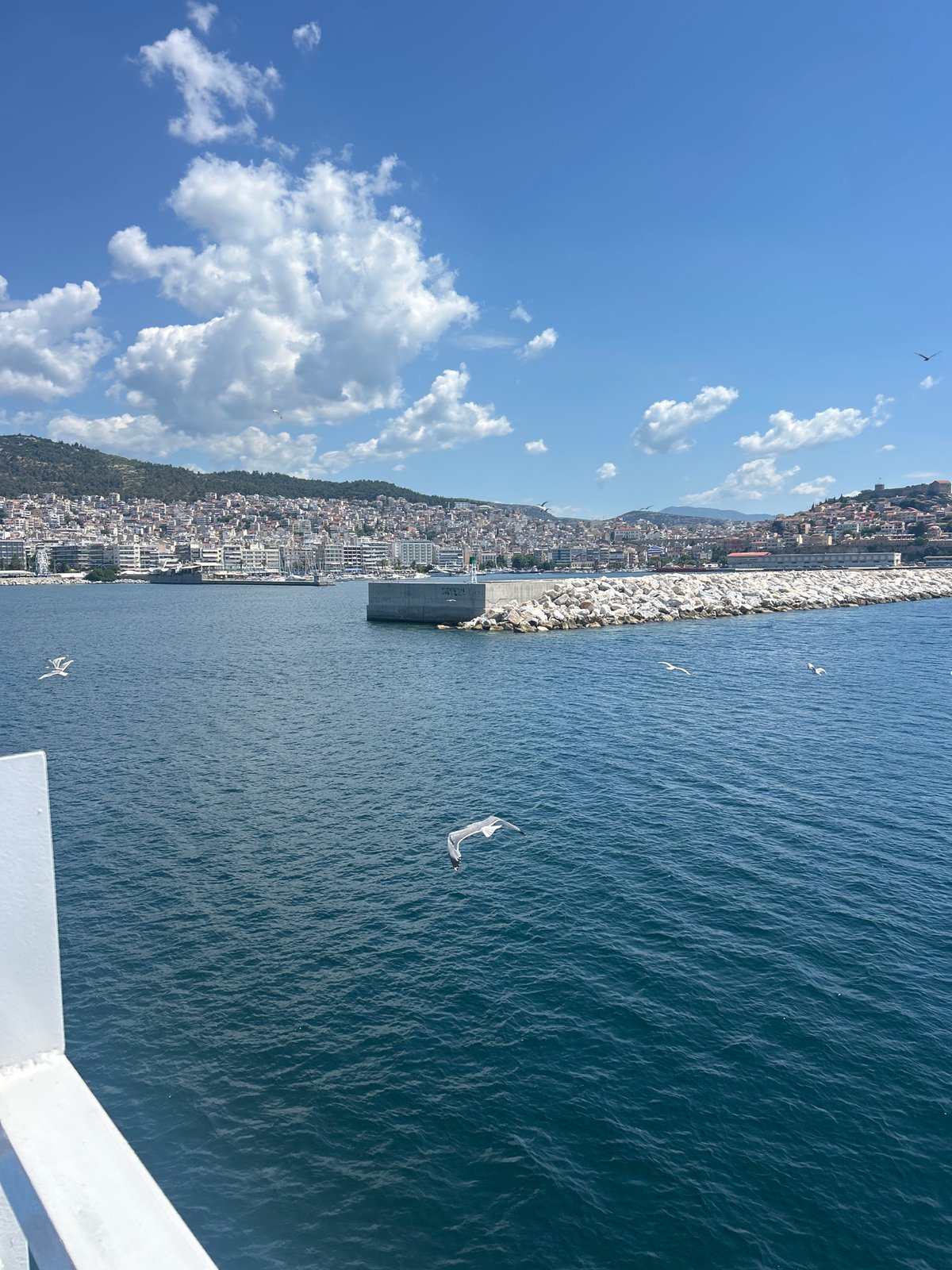 Ferry crossing toward a hillside coastal city on a sunny day