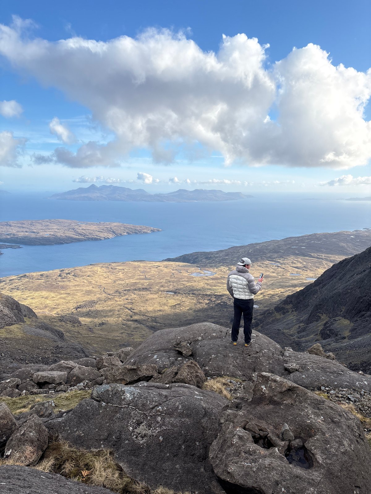 Person stands on rocky outcrop overlooking Scottish coastal landscape