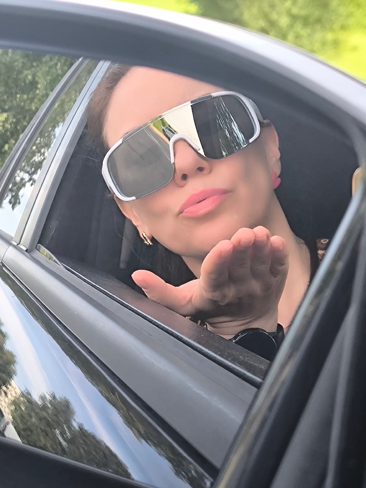 Leaning out a car window in Riga, white sunglasses on