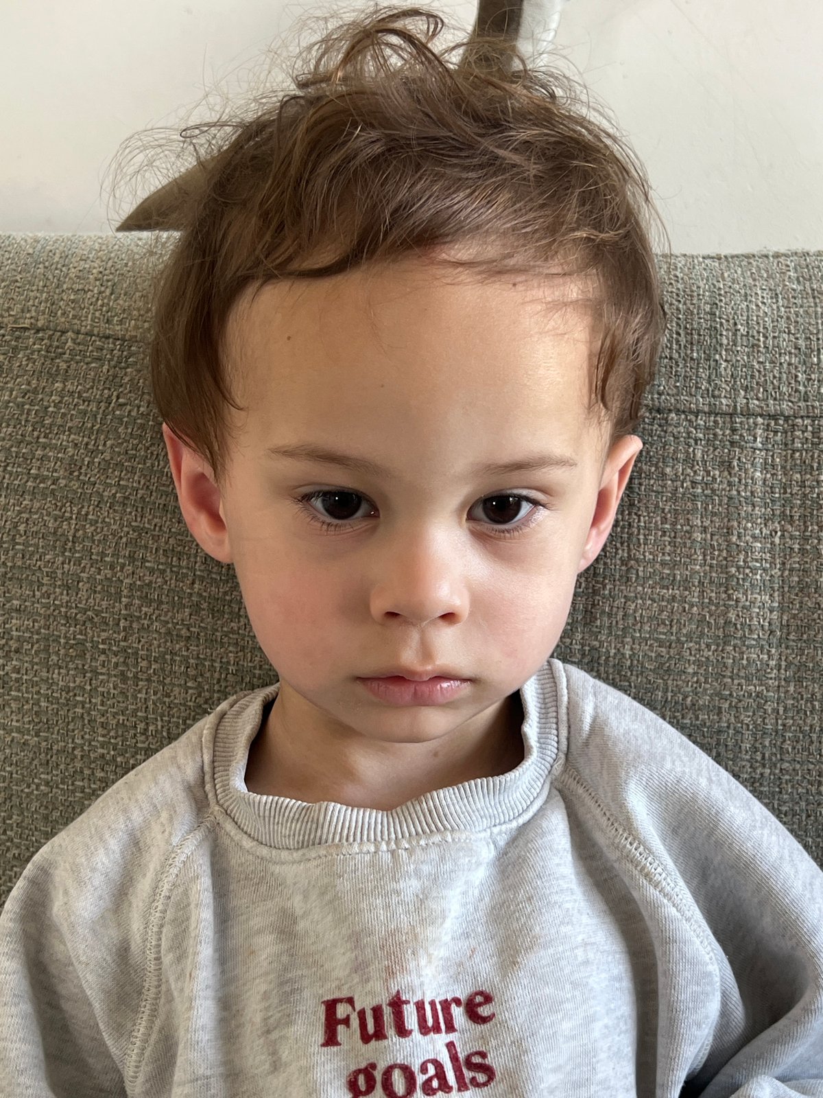Toddler in grey sweatshirt rests on couch in Kiryat Bialik