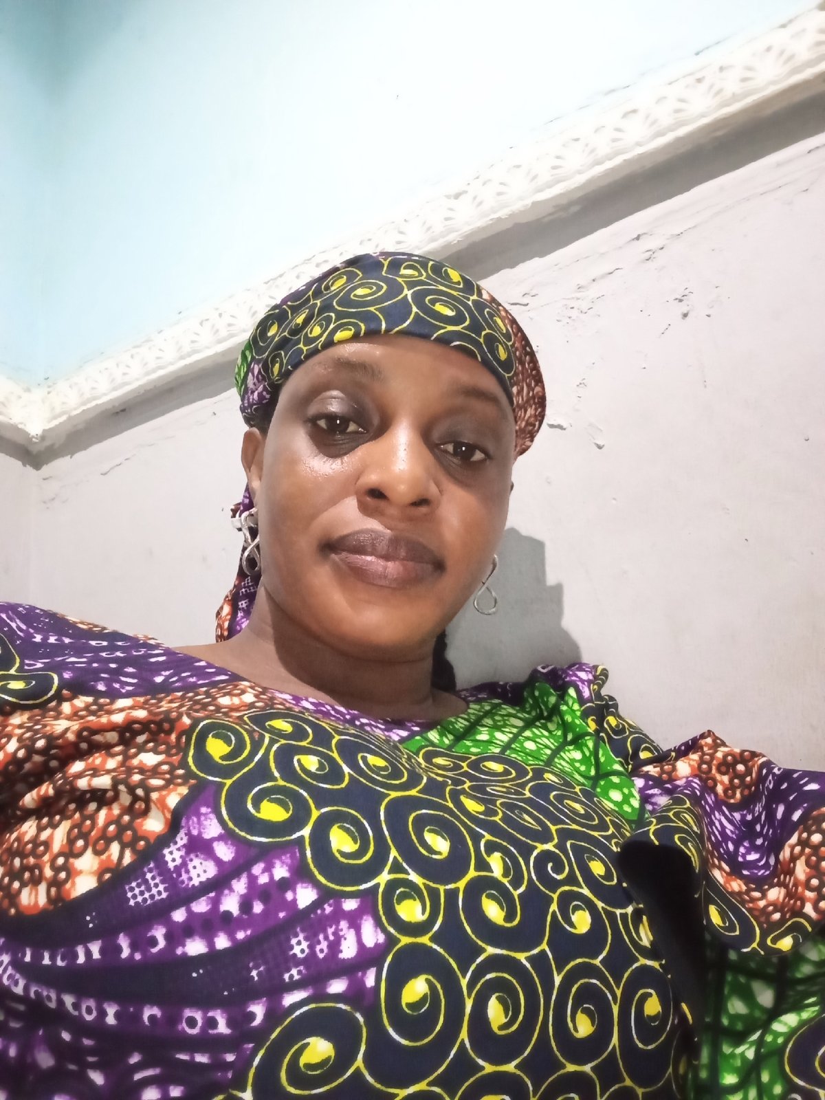 Woman in colorful headscarf photographed against patchy wall