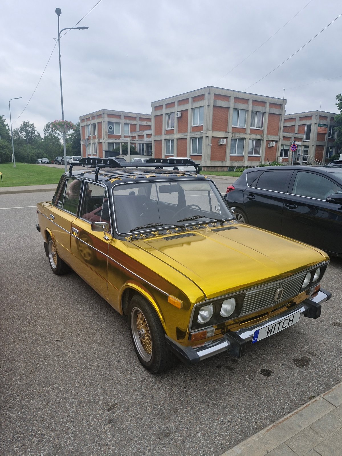 Chrome-wrapped Soviet sedan parked outside Brutalist buildings in Latvia