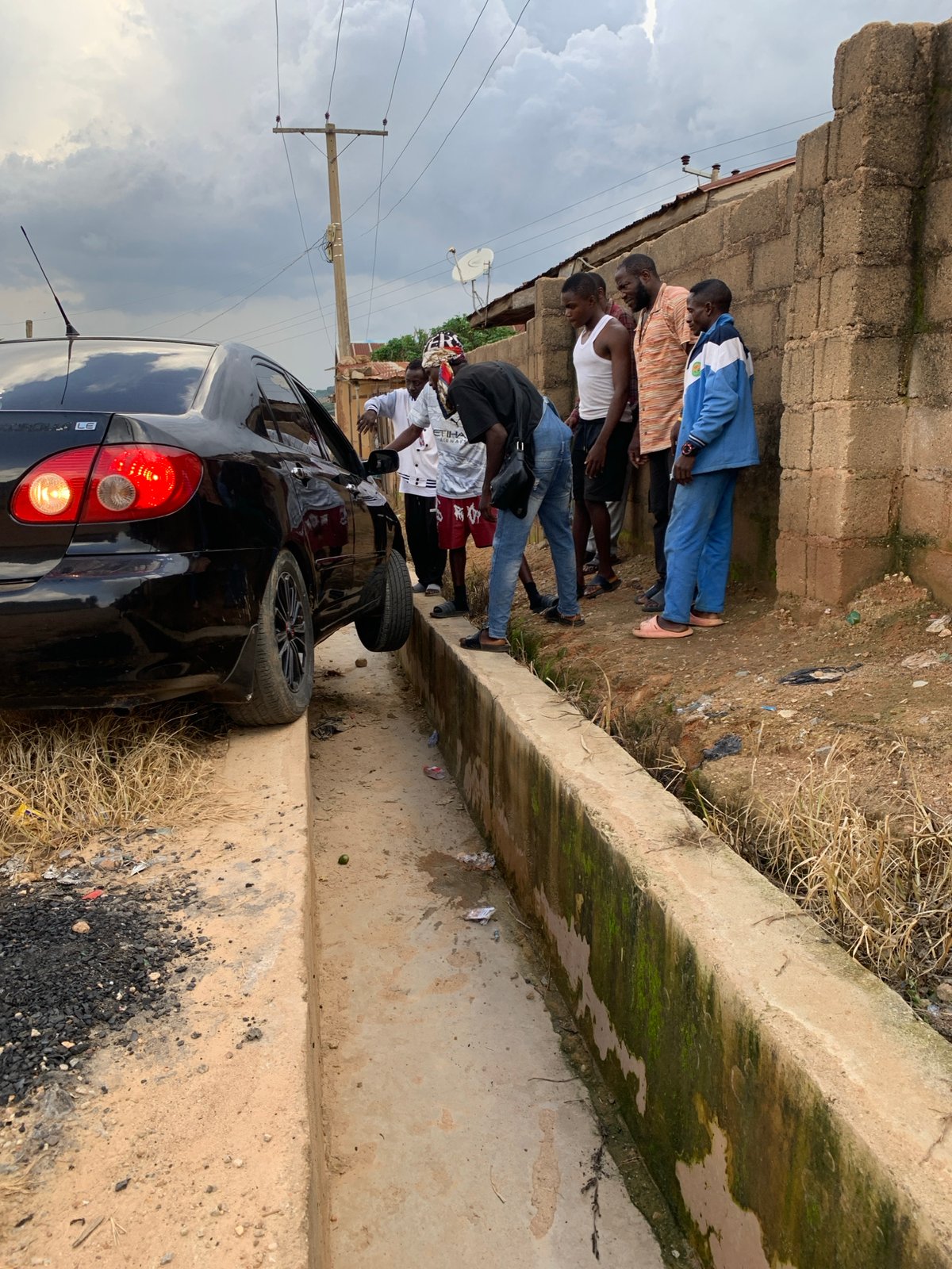 Car stuck in drainage ditch draws crowd in Jos