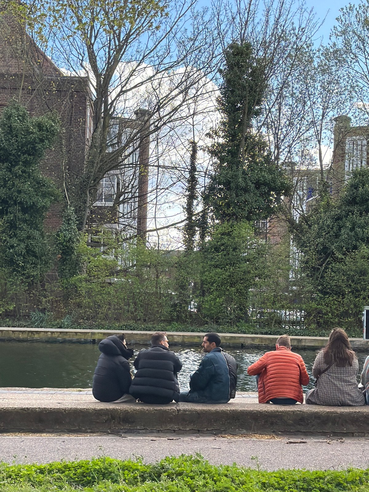 Four people sit by London canal in cool weather