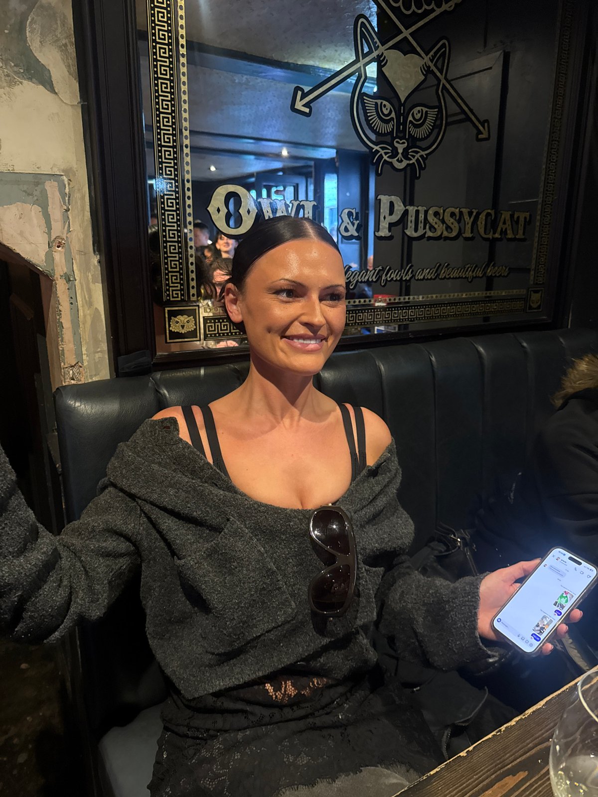 Woman photographed smiling with smartphone in bar setting