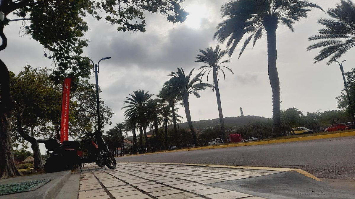 Coastal Venezuelan town at dusk: scooters, palms, and a lighthouse