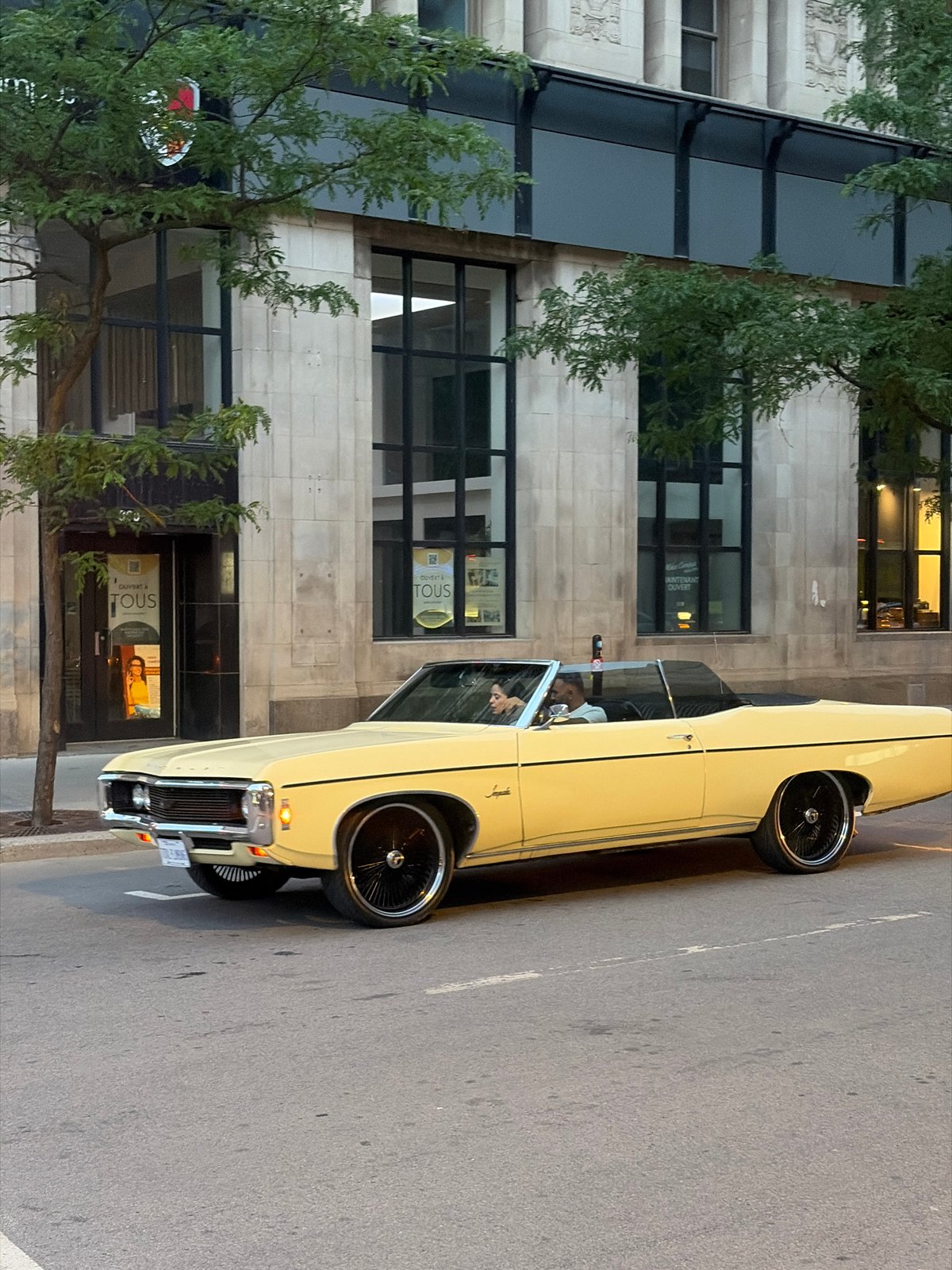 Vintage convertible drives through twilight Montreal streets