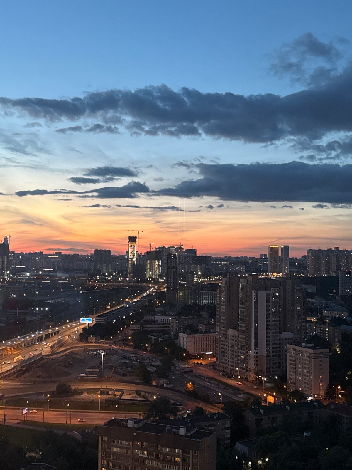 City skyline at dusk, red-lit skyscraper under a gradient sunset