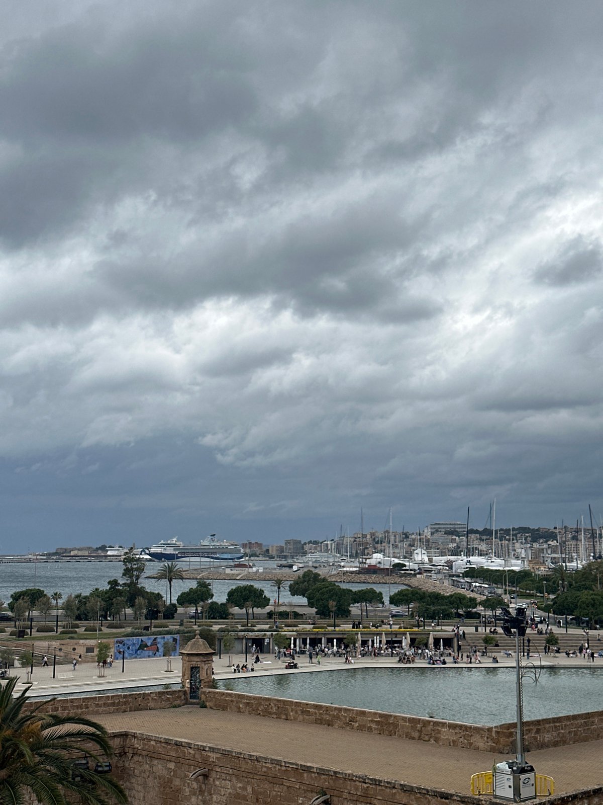 Tourists photograph Palma Cathedral and harbor views under cloudy skies
