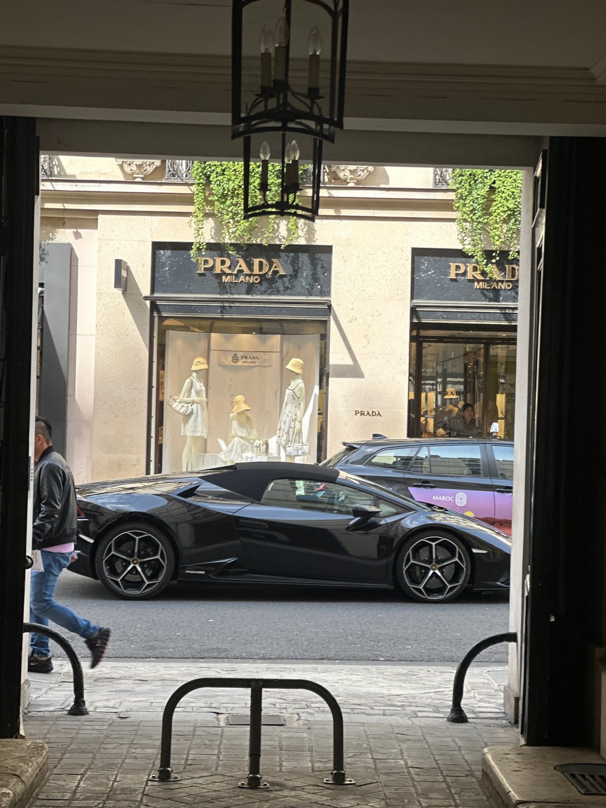 Man lies on Paris street near luxury car, Prada store