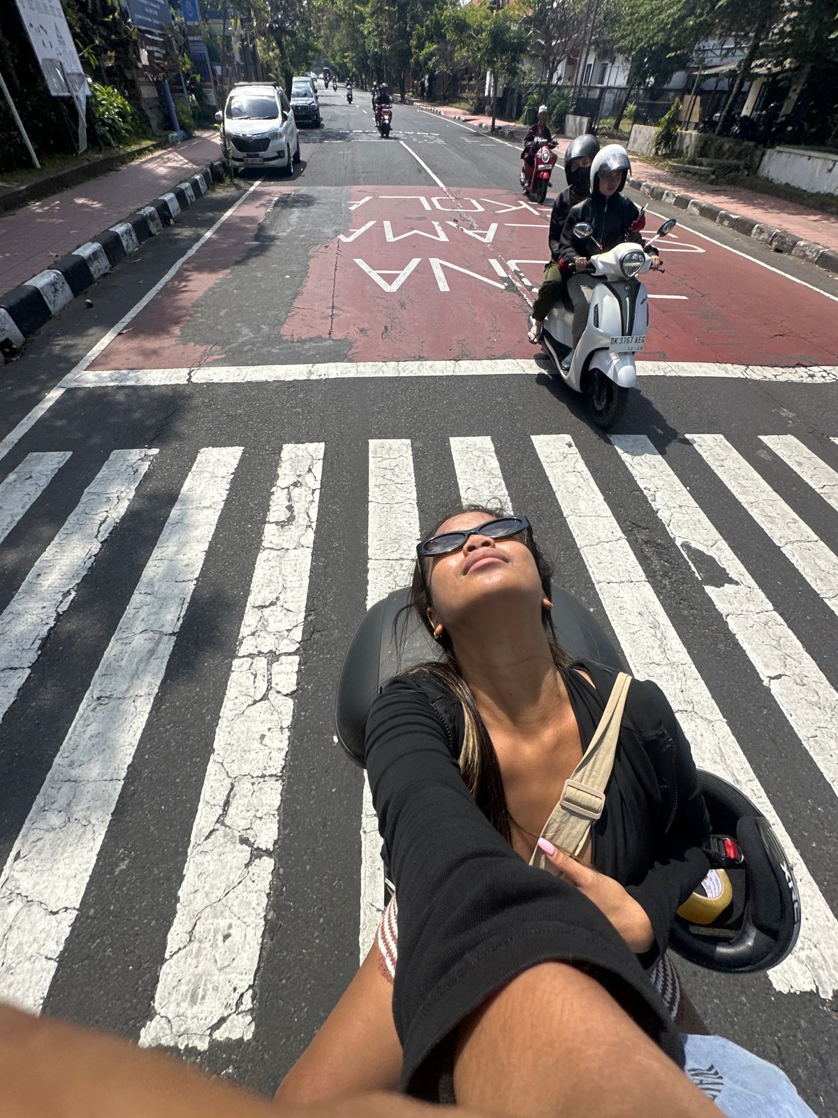 Woman rides motorcycle through Denpasar streets on sunny morning