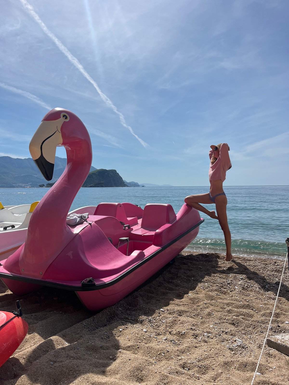 Woman poses with pink flamingo paddle boat on Budva beach