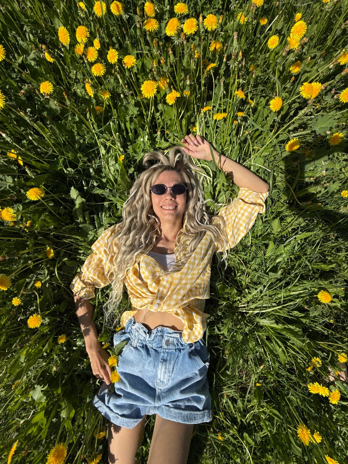 Woman relaxes in dandelion field wearing checkered shirt