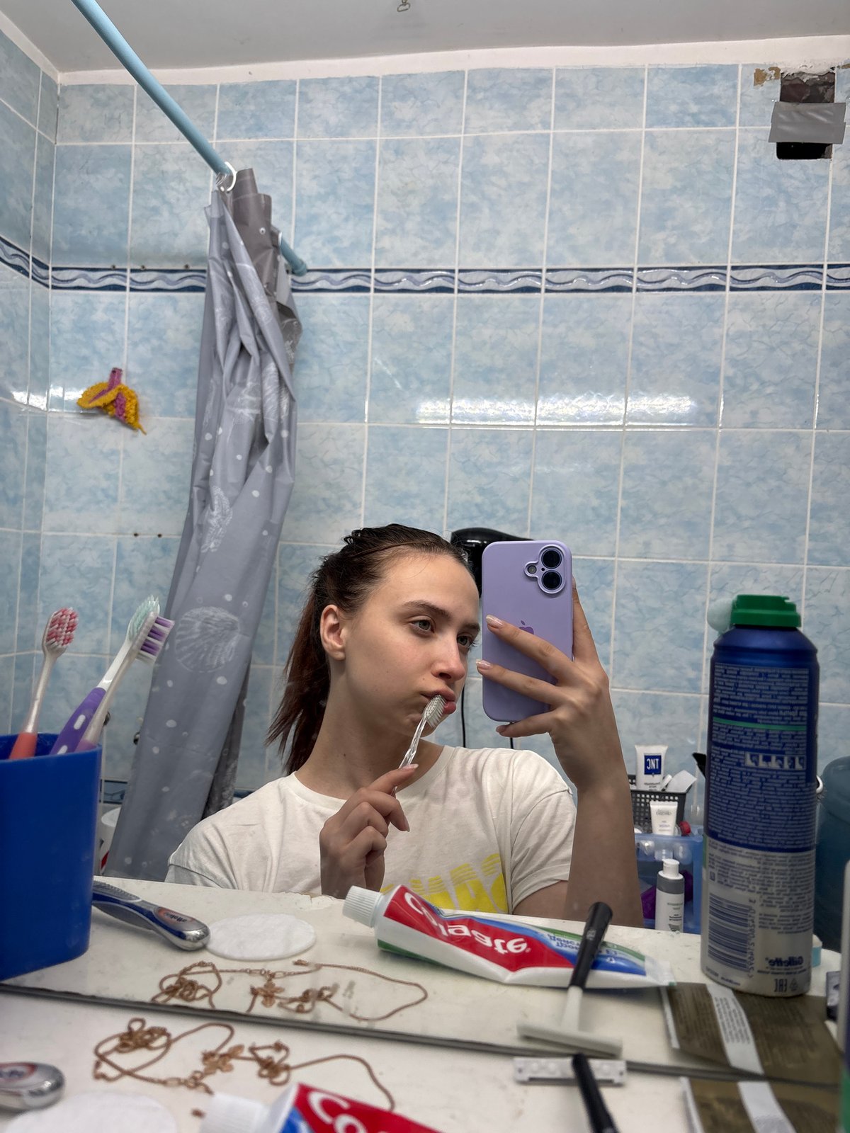 Person takes mirror selfies with purple phone in Russian home