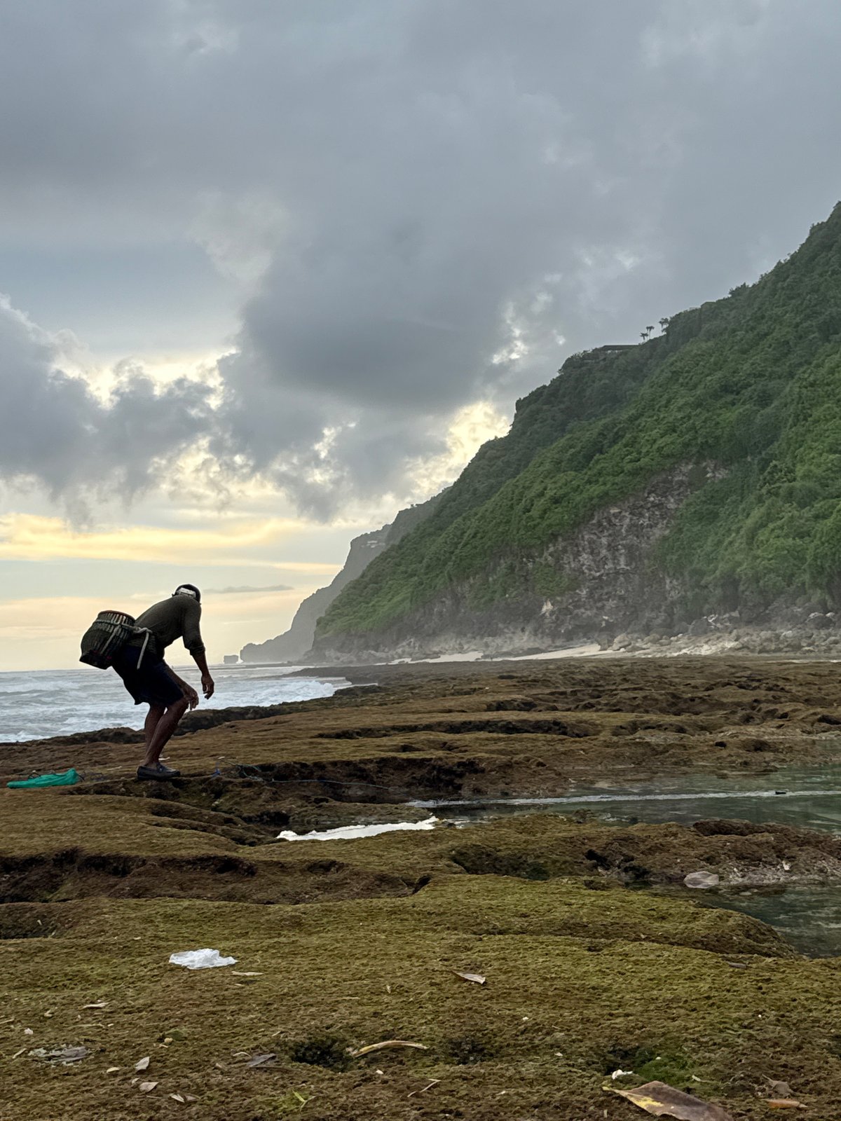 Person observed on rocky shore near clifftop structures in Pecatu