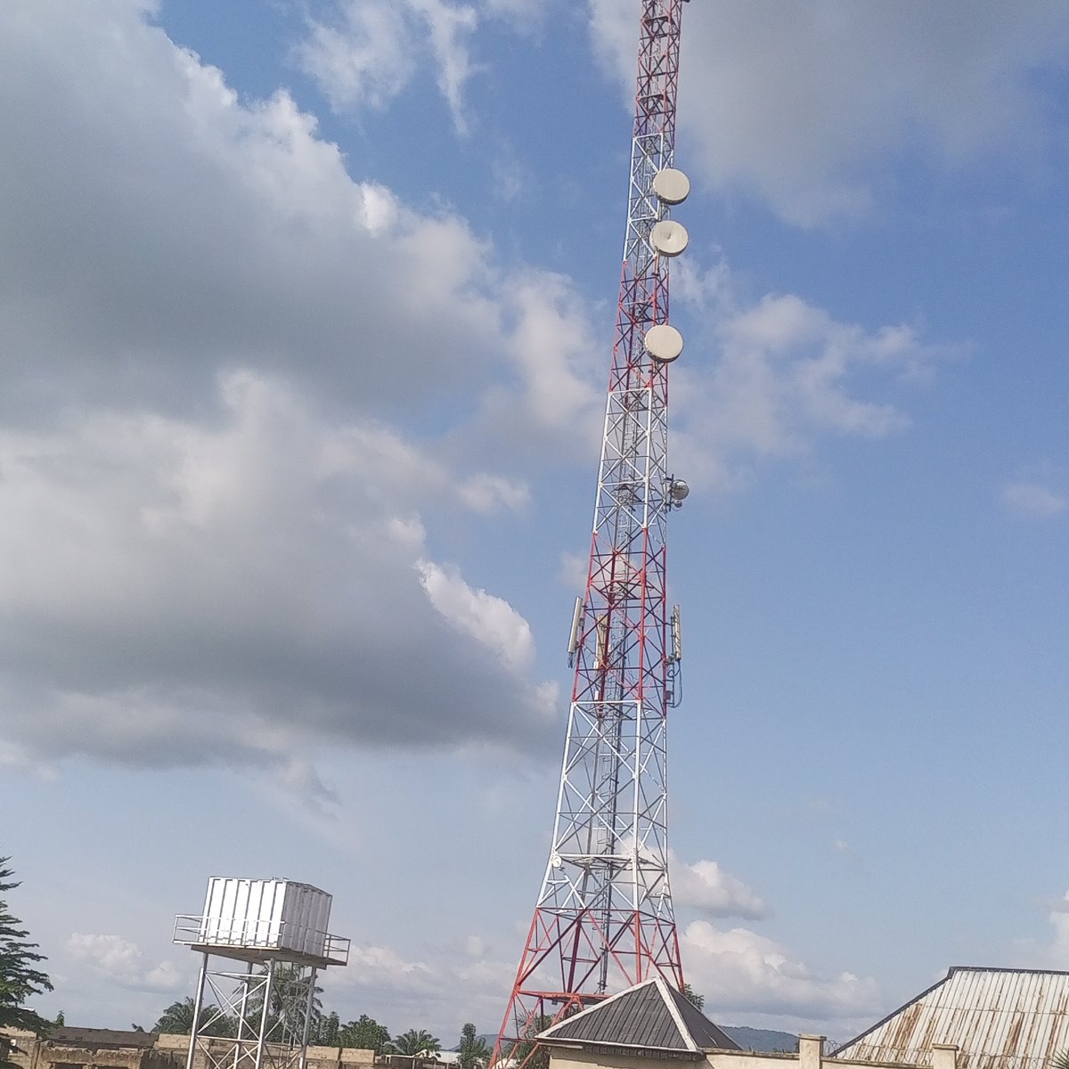 Red and white telecom tower with satellite dishes in Serti, Nigeria