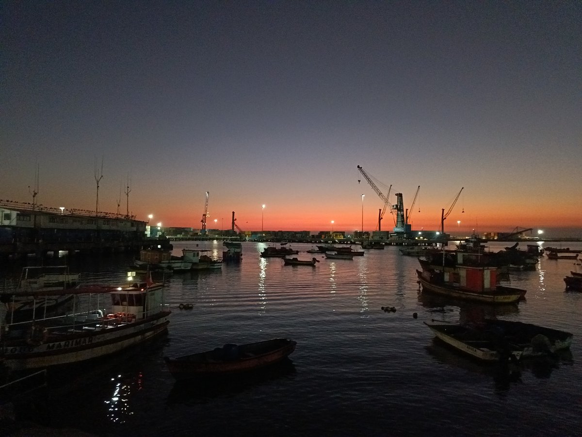 Arica harbor at dusk, boats and cranes under a sunset sky