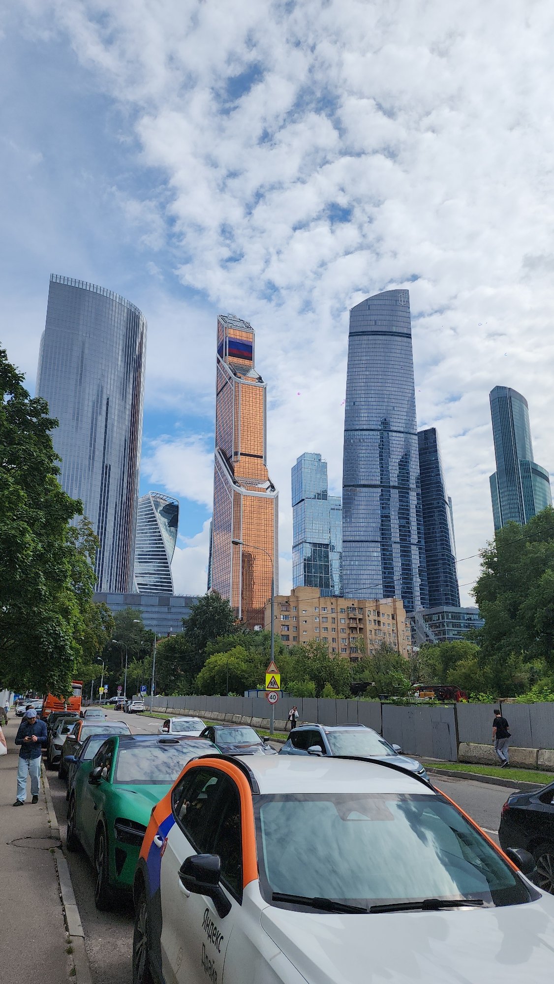 Green Xiaomi SU7 parked on Moscow street, skyscrapers behind