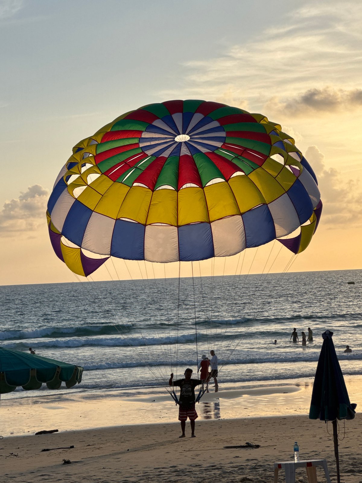 Karon Beach at sunset — parasailing, shoreline crowds, golden hour