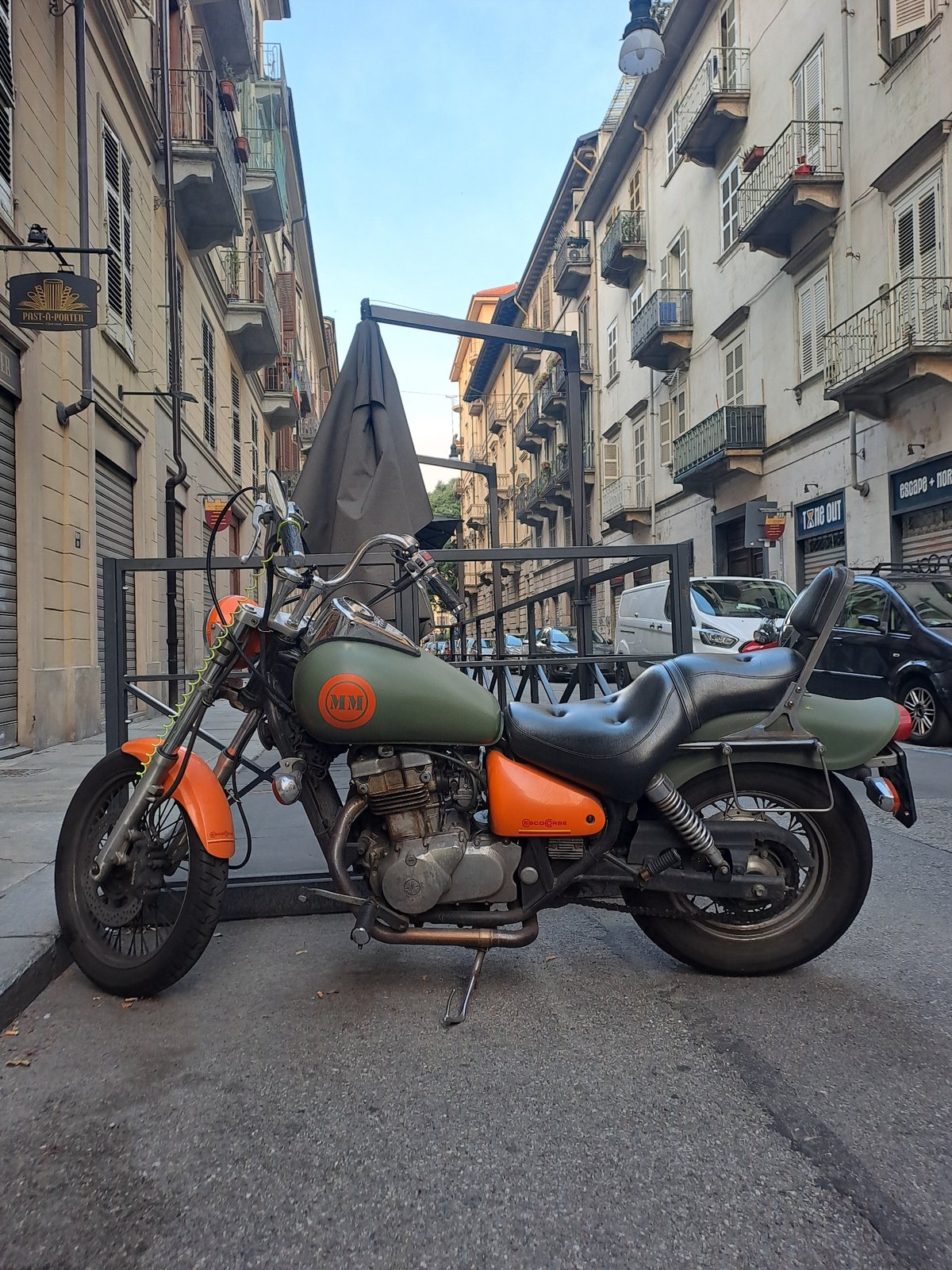 Custom motorcycle and red Vespa parked on a Turin street