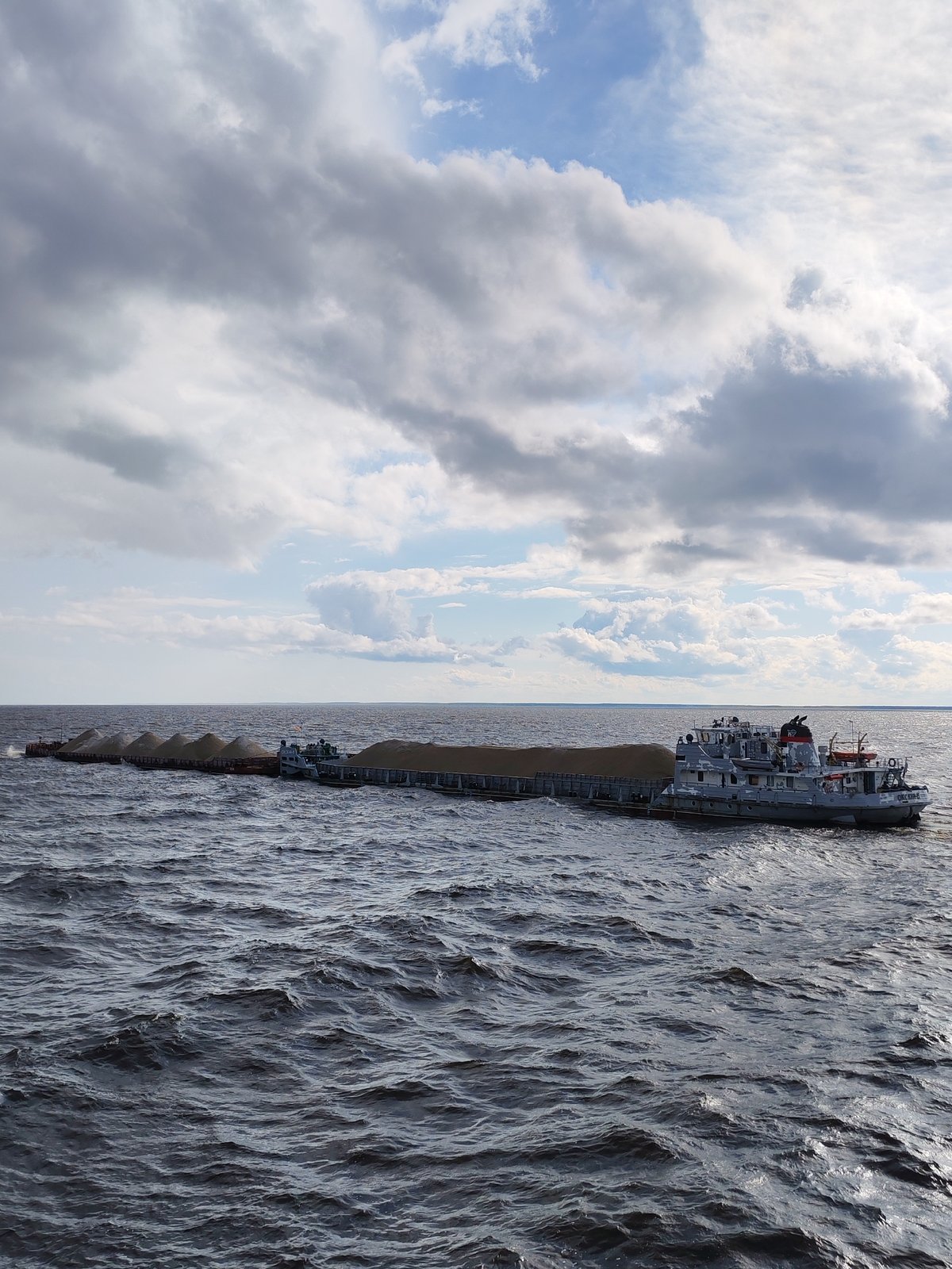 Cargo ships and barges crossing open water on a cloudy day