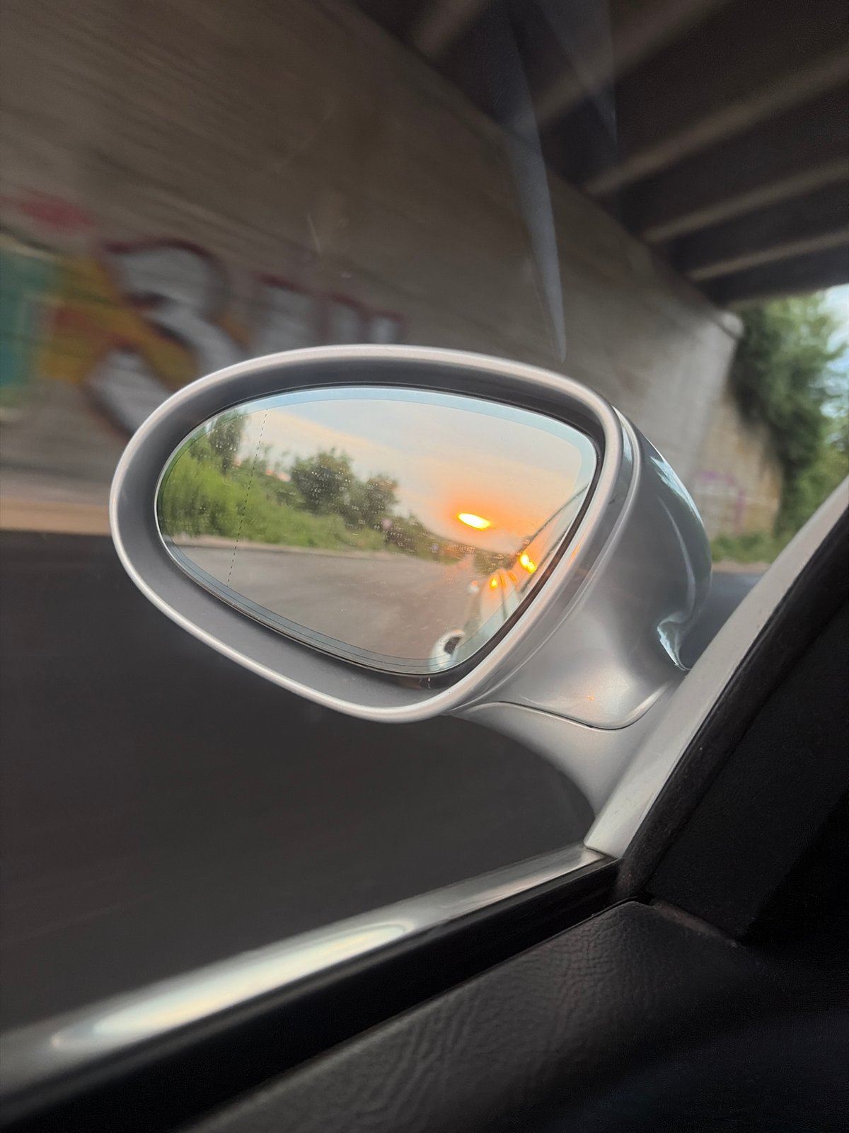 Sunset caught in a rear-view mirror under a graffiti overpass