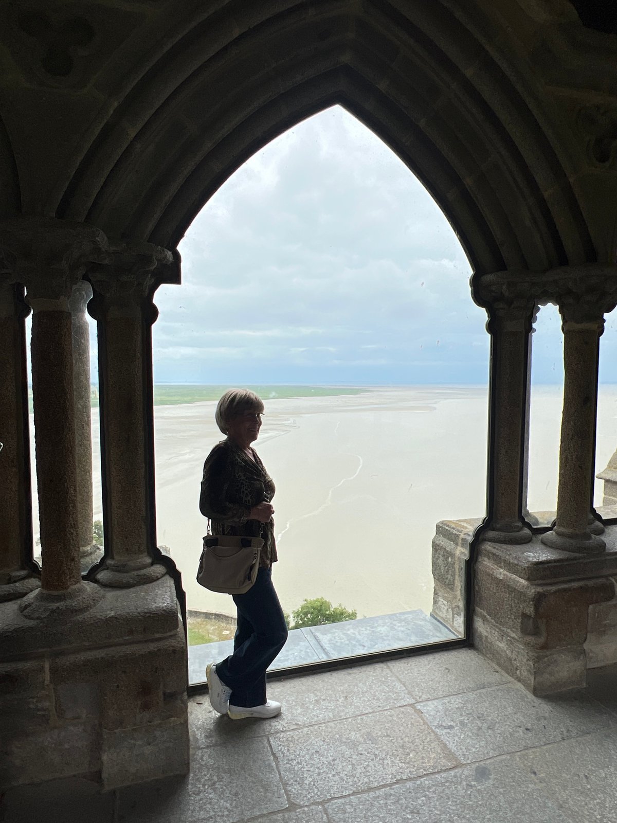 Woman silhouetted in stone archway observing landscape in Hirel
