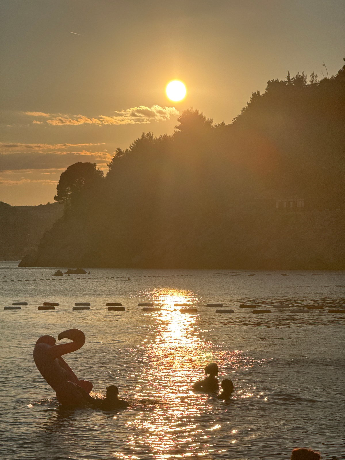 Kamenovo Beach at sunset, crowds, calm water, and an abandoned building nearby