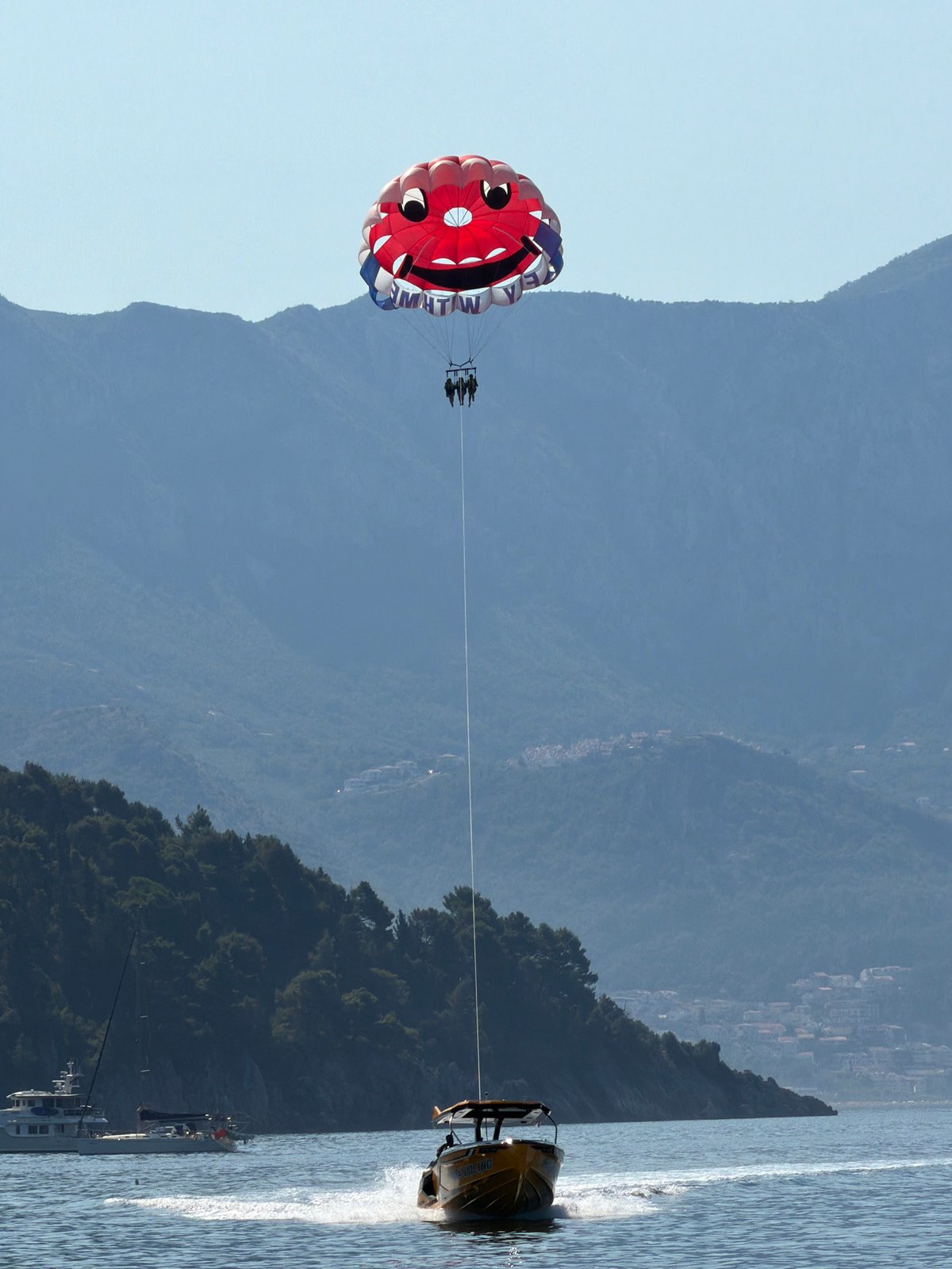 Busy coastal day: parasailing, packed beaches, and boat traffic