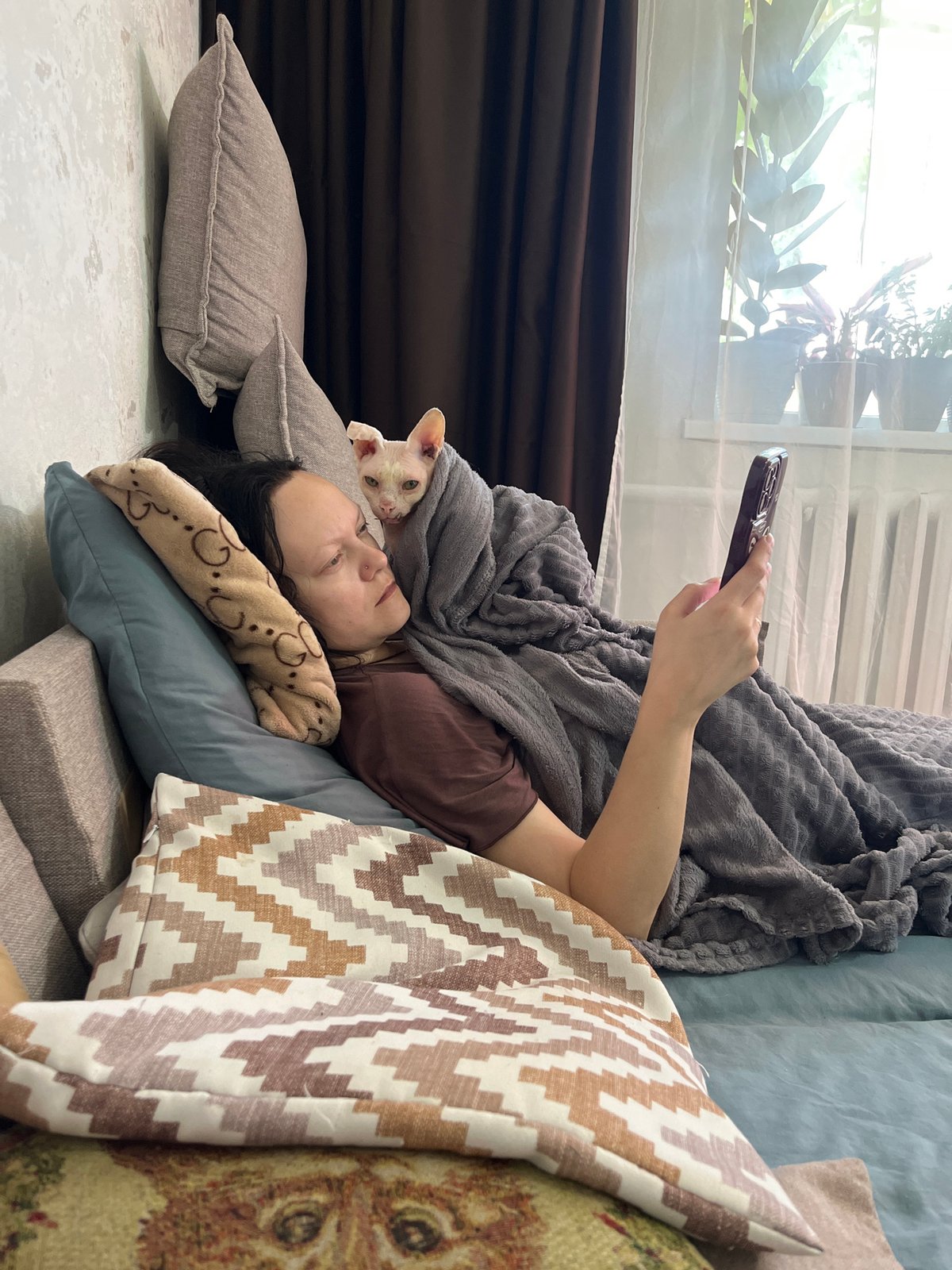 Person relaxes with cat while using phone indoors