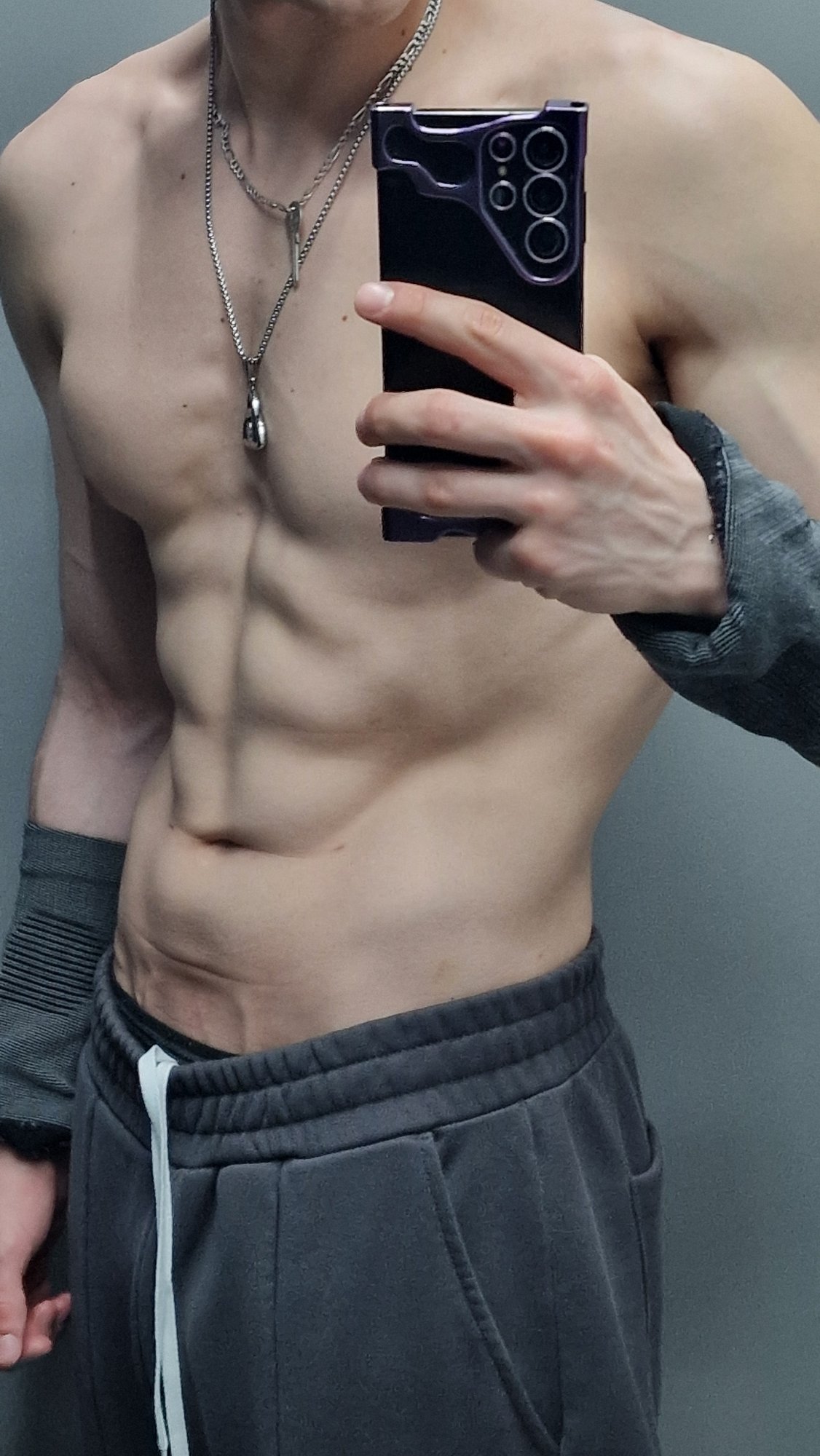 Shirtless individual photographed with smartphone at unknown location