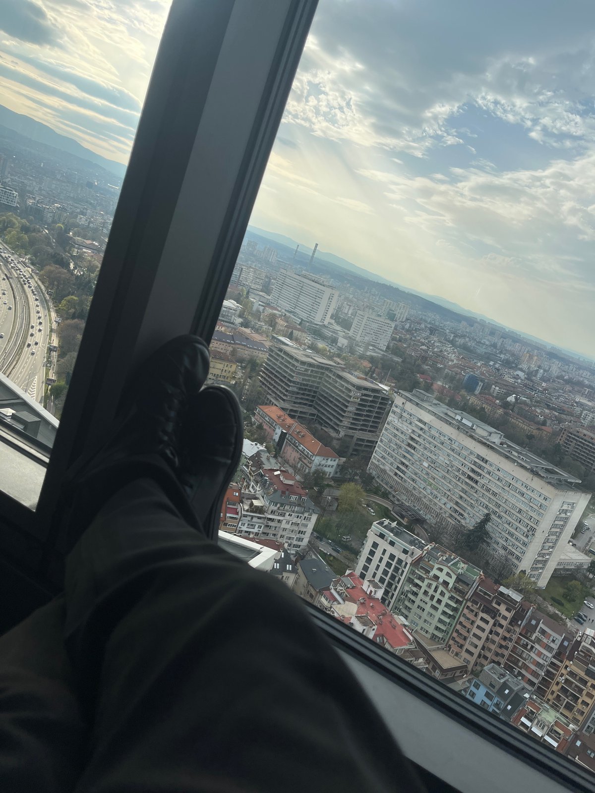 Person rests feet on window sill overlooking Sofia cityscape