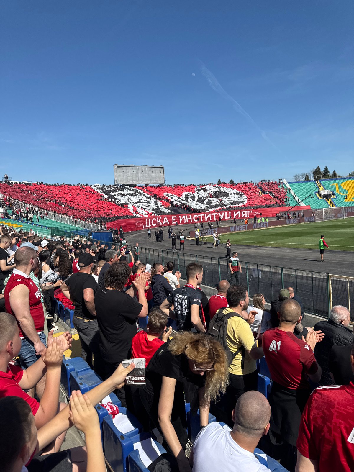 Soccer stadium packed with red-clad fans during daytime match