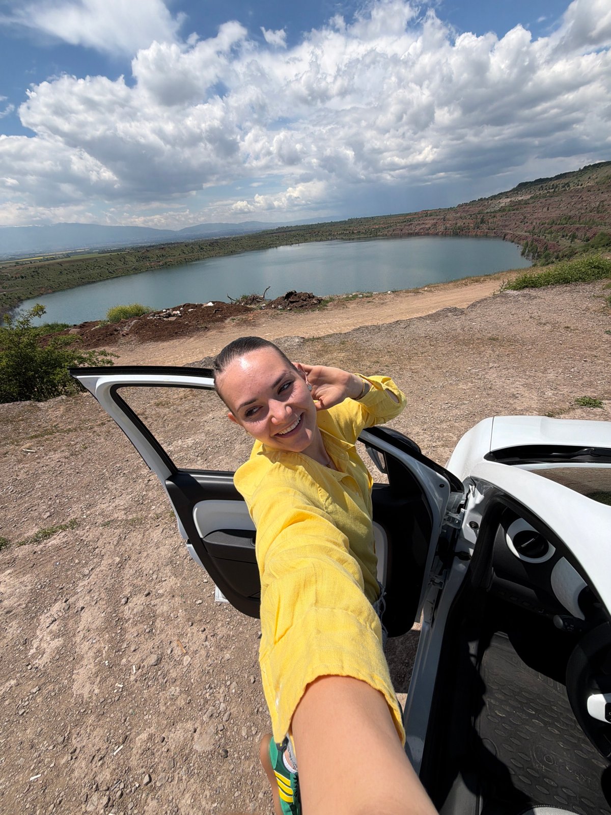Woman poses by white car at scenic lakeside near Sofia