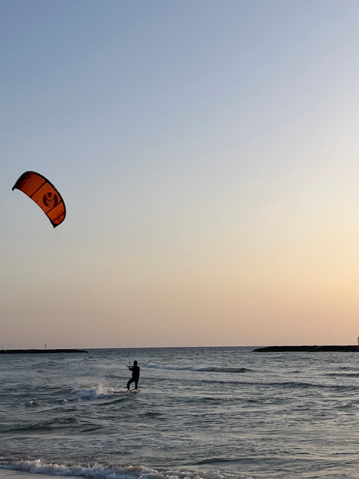 Kitesurfer spotted with orange kite at unidentified coastal location