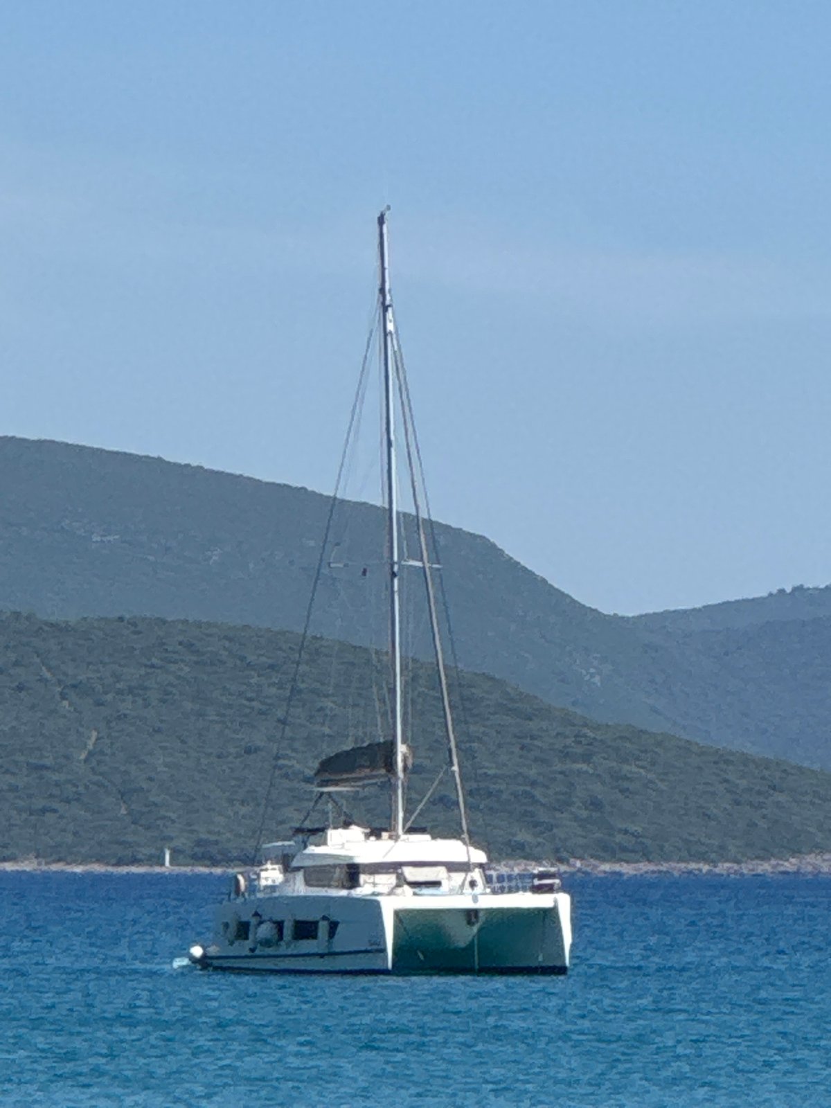 Lazy afternoon on a rocky beach with a catamaran anchored offshore.