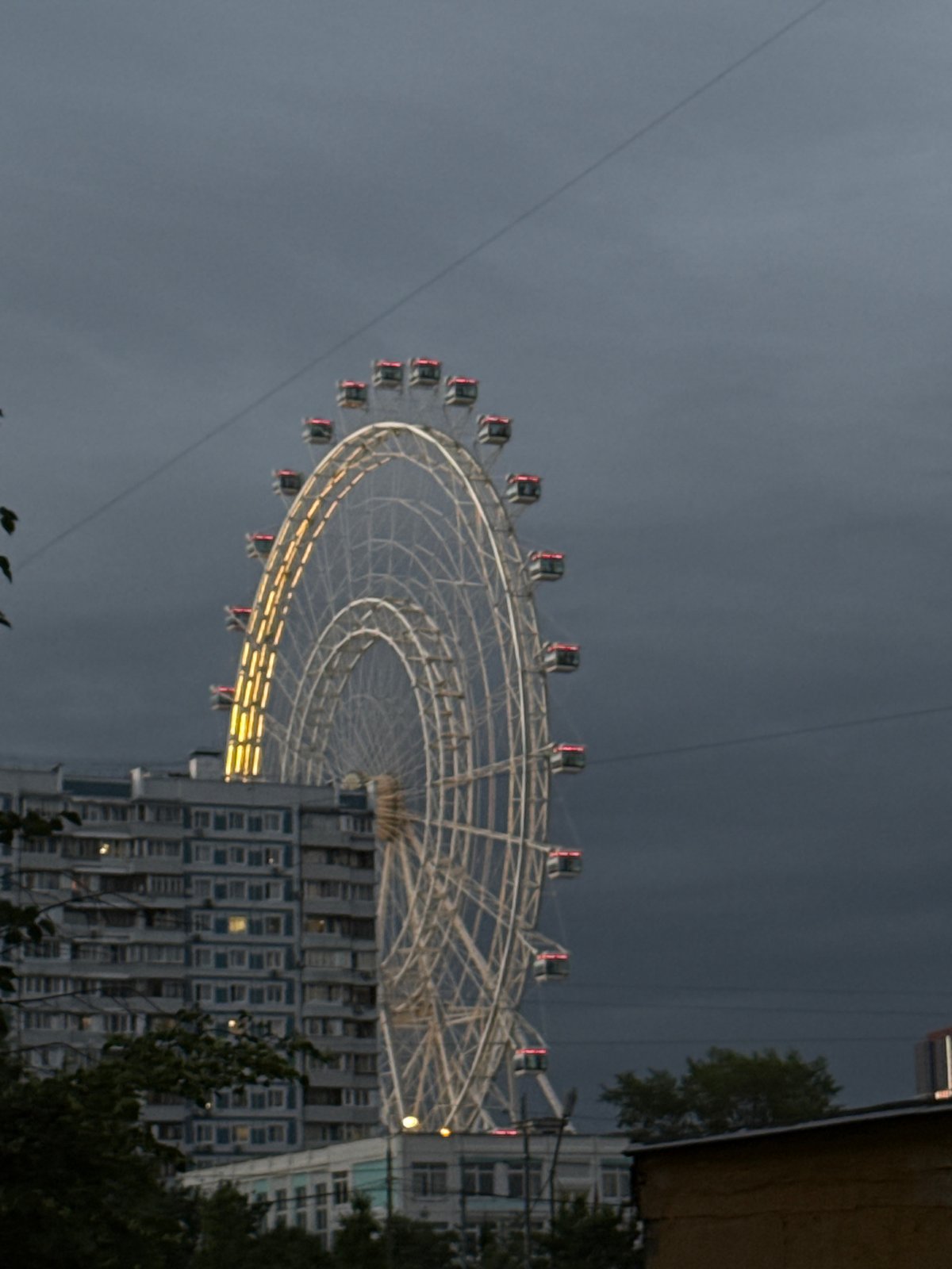 Illuminated Ferris wheel beside apartment building in Dolgoprudny evening