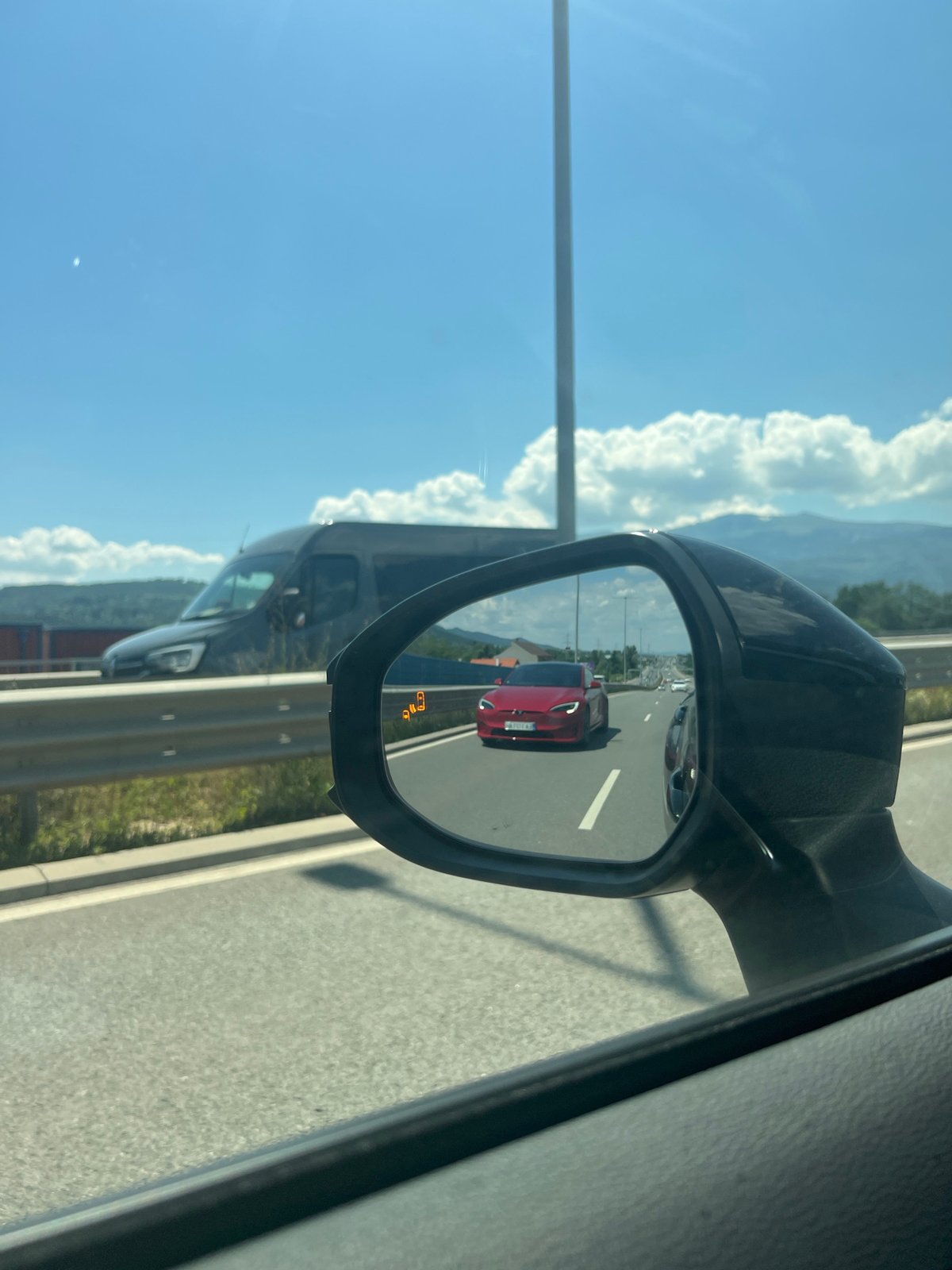 Red Tesla on a Sofia highway, seen through a side mirror