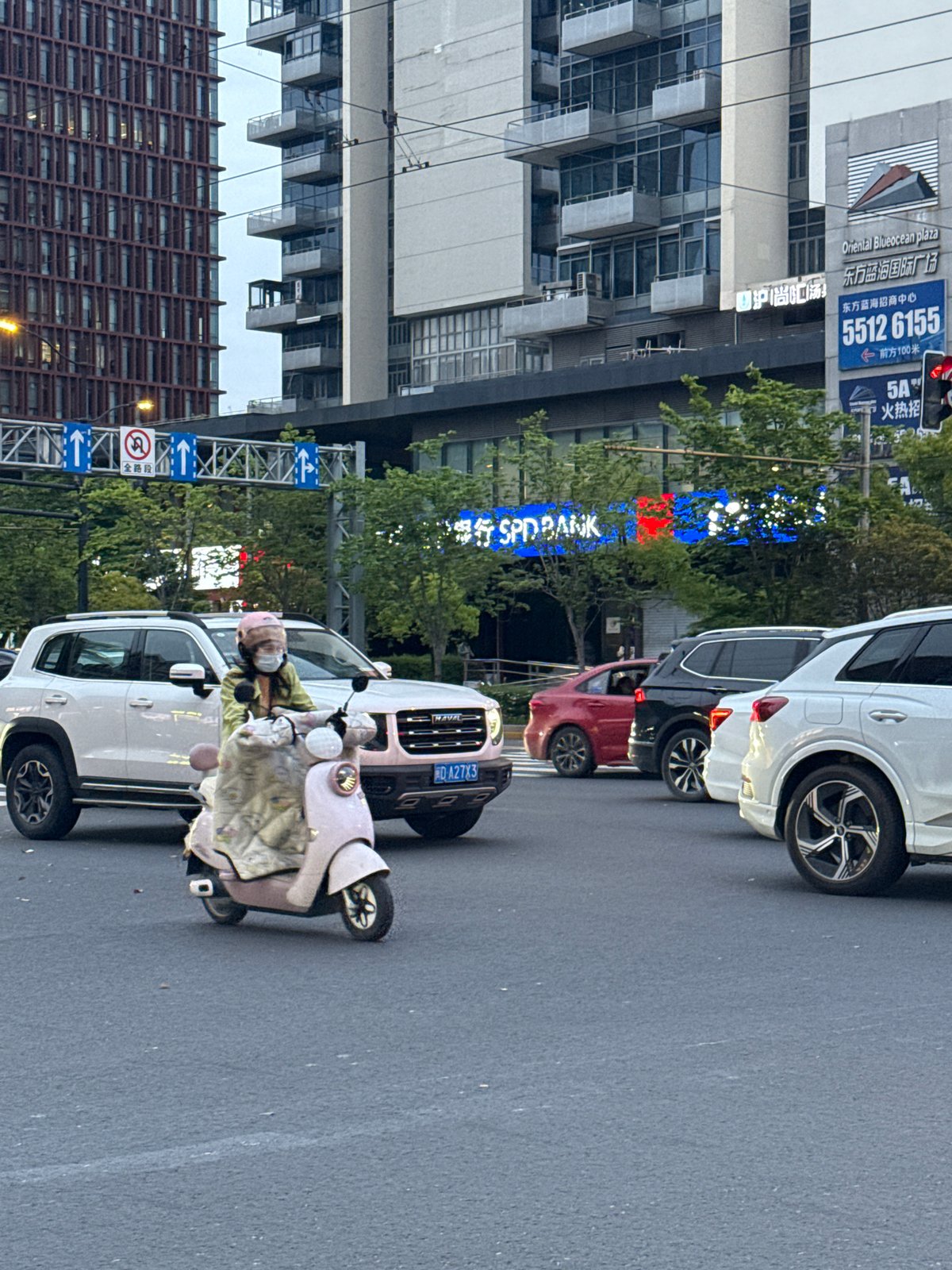 Pink scooter rider navigates busy Shanghai intersection under overcast skies