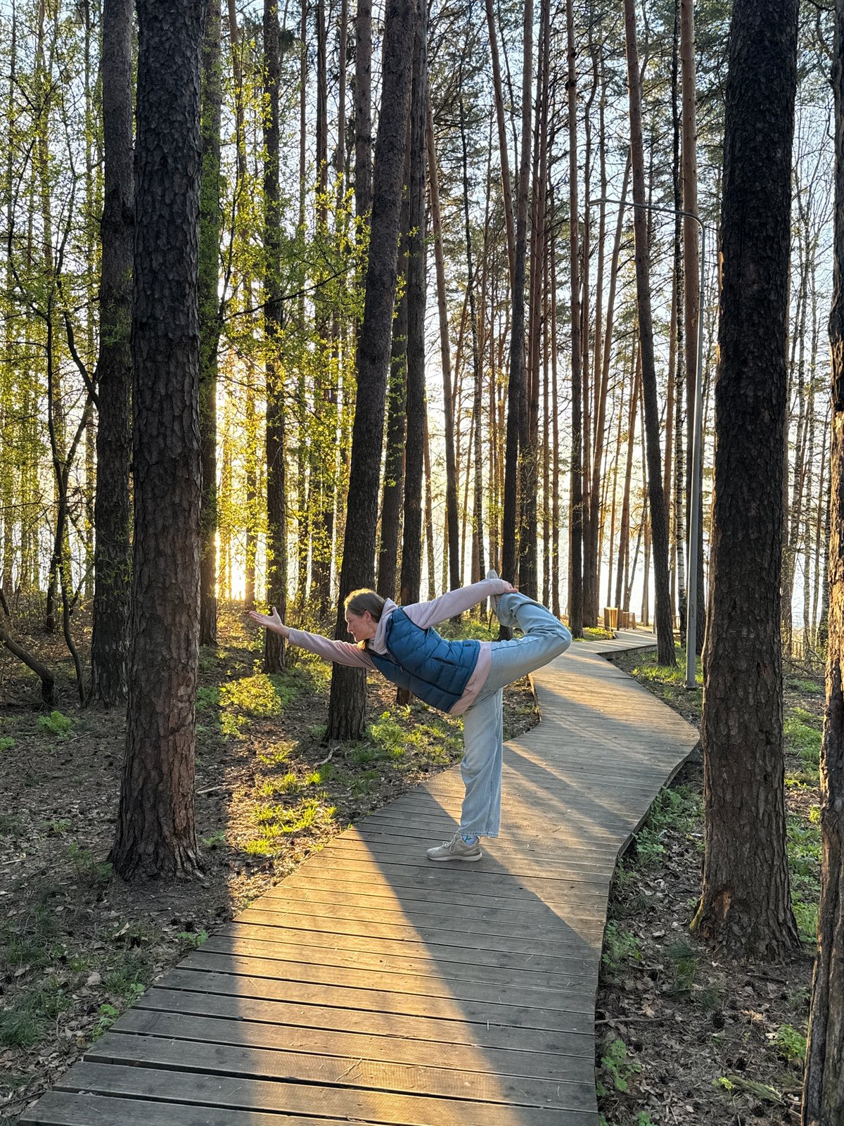 Woman practices yoga on forest boardwalk near water in Russia
