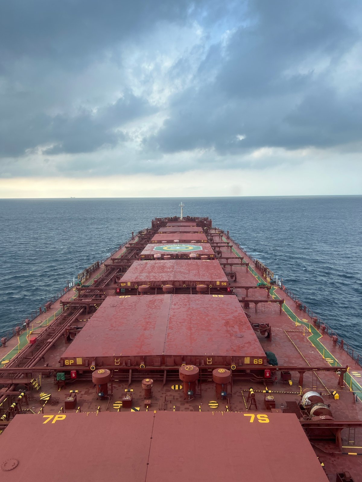 Red bulk carrier at sea, deck hatches and cargo markings visible.