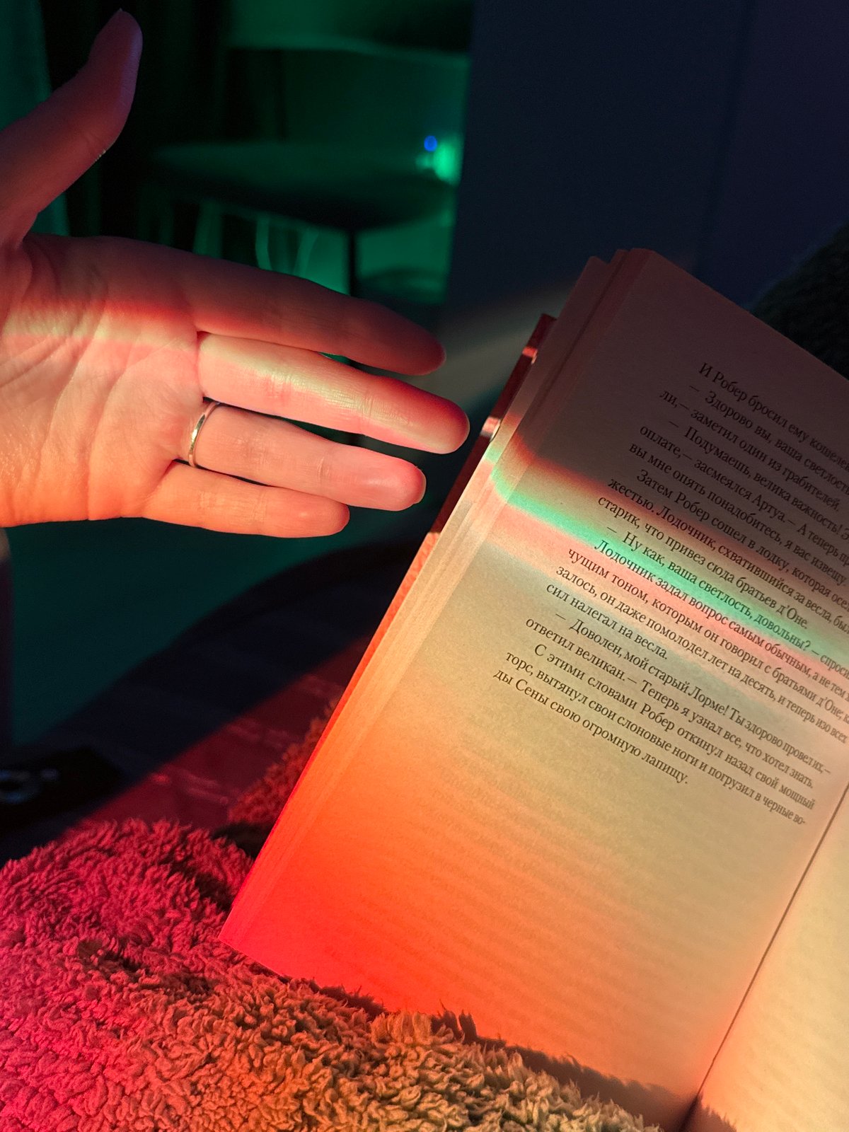 Person reads Russian book under rainbow lighting on blanket