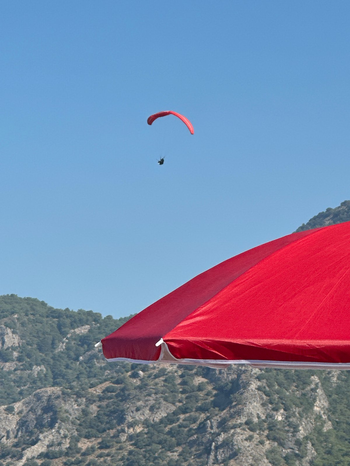 Sunny morning on Fethiye's pebble beach with paragliders above