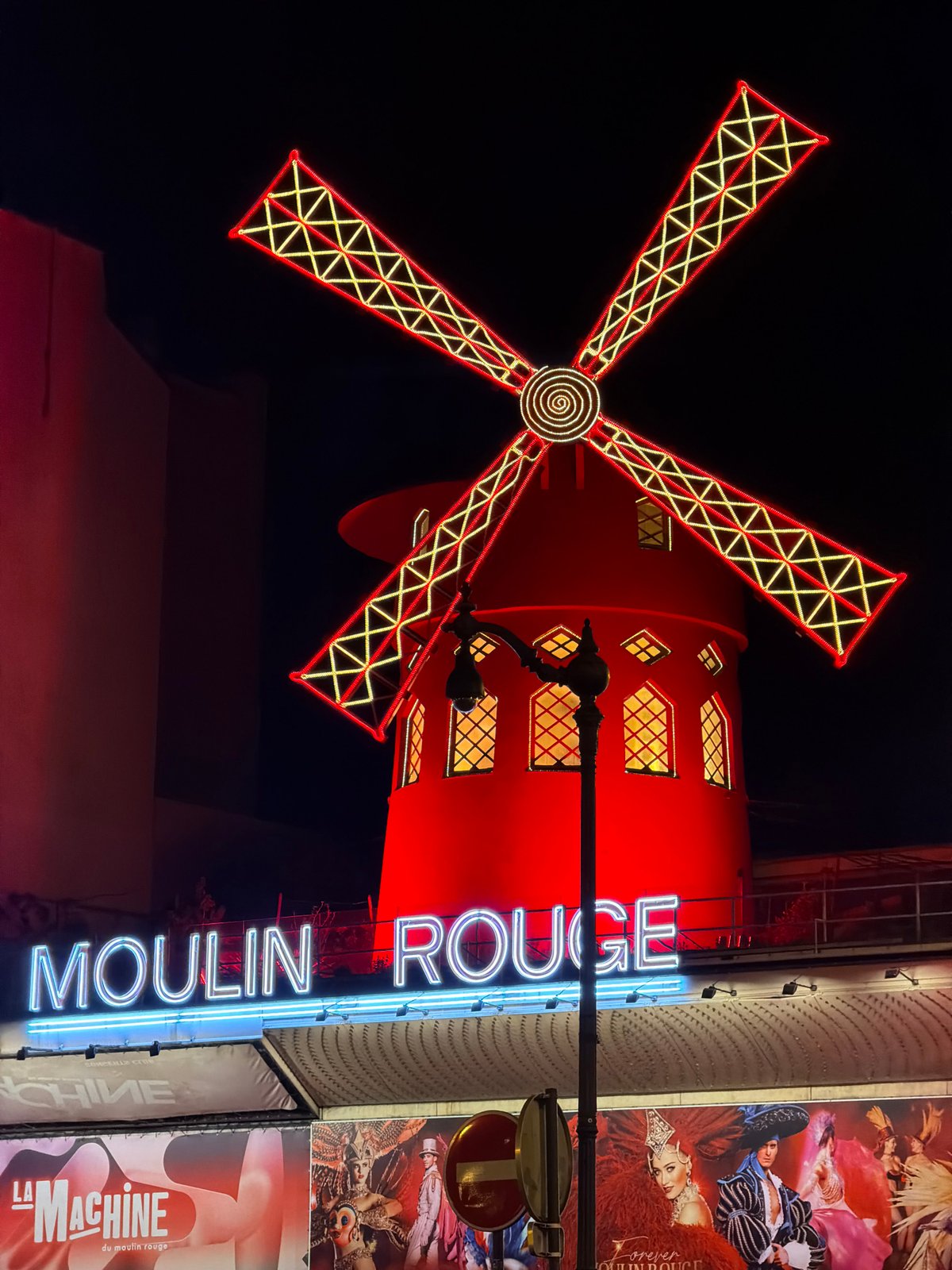 Evening street life documented around illuminated Moulin Rouge, Paris