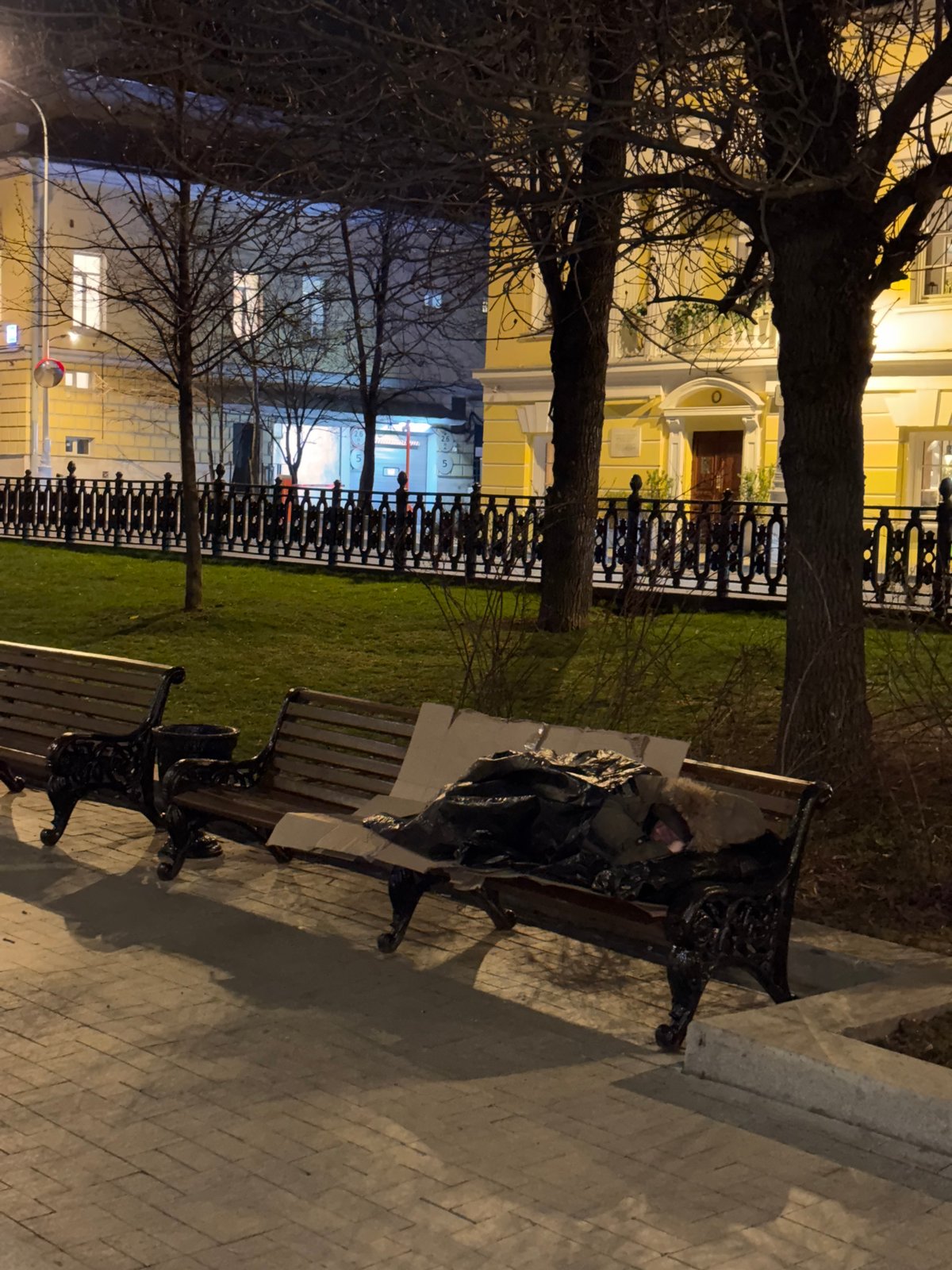 Person sleeps on Moscow park bench covered by tarp