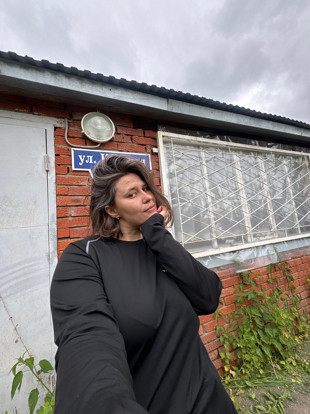 Woman takes playful selfies with plants near brick building