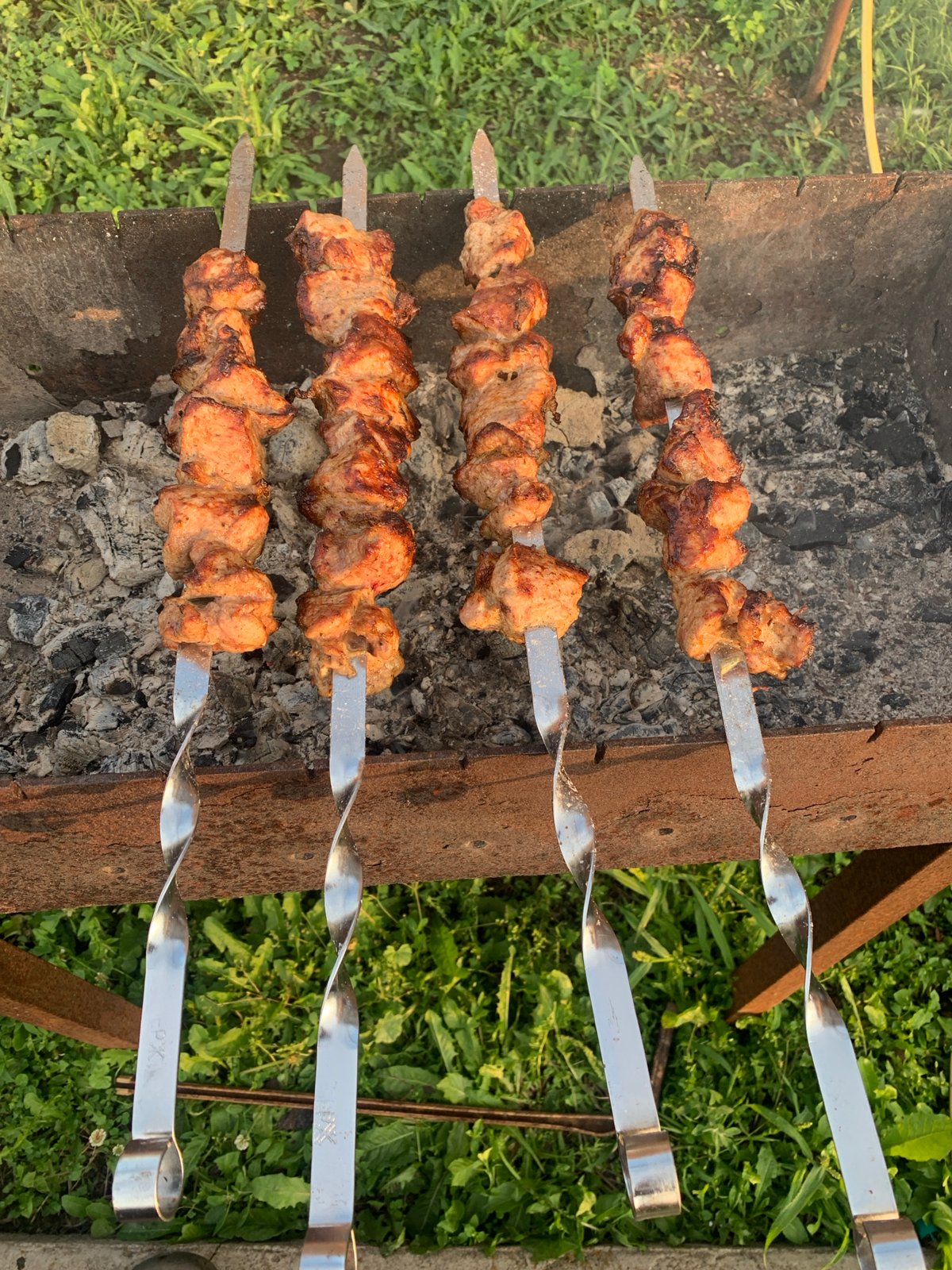 Cubed meat on spiral skewers over a barbecue grill.